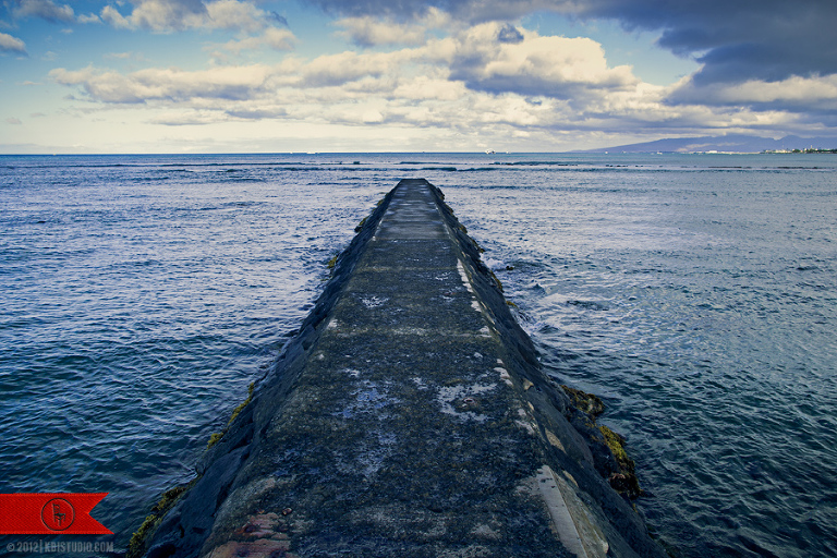 The distant ocean horizon of Waikiki beach in Hawaii skyline off a stone pier.
