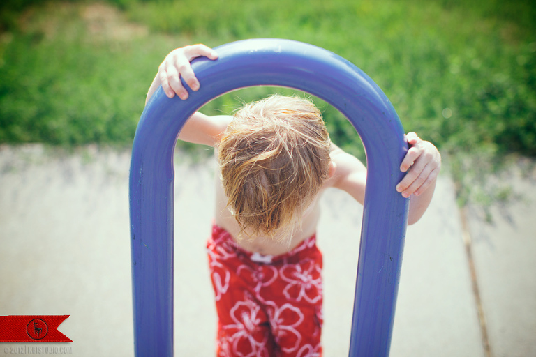 3-year-old sticking his head through a blue bike rack at the local playground/splash park.